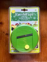 Photo of new FreshFare Veggie Slicer in sealed retail packaging showing the green round slicer with black blade and yellow knob.