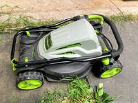 Compact black and gray Yard Works LawnMaster 2-in-1 electric lawn mower with bright green wheels and parts, folded handle, placed on concrete