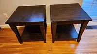 Front view of two wooden IKEA end tables with lower shelves, showing dark finish and scratches.
