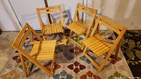 Four wooden folding chairs arranged on a patterned rug, showing the front and side profiles.