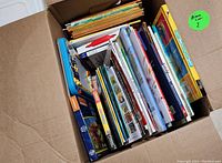 Box filled with various children's books showing the top edges and some colorful covers, packed tightly in the box.