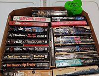 Photo of a box containing suspense paperback novels by Stephen King, Dean Koontz, Tom Clancy, Michael Connelly and others. Books show heavy wear with creased and torn spines and covers.