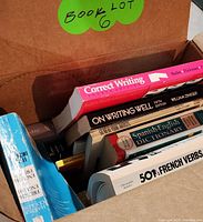 Photo of six books stacked in a box labeled 'Book Lot 6', showing titles including Correct Writing, On Writing Well, Spanish-English Dictionary, 501 French Verbs, and others.