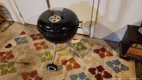 Closed view of the round black Weber charcoal grill on tripod legs and wheels, seen from above.