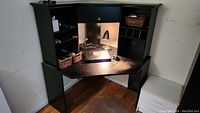Wide angled photo of the black laminate corner desk showing the worn desktop surface, drawer, cabinet, multiple shelves and cubbies on the hutch.