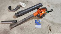 Complete view of Husqvarna leaf blower with tubes and user manual laid out on concrete floor.