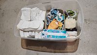 Top-down view of a plastic bin containing white cloth diapers, assorted patterned cloth diapers, swim diapers in packaging, white absorbing pads, washcloths, and various small cloth accessories.