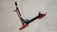 Photo of Railz snow scooter toy showing full side view with red skis and black handlebar on floor.