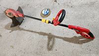 Full view of the red Homelite corded string trimmer laying on a concrete floor with the partial roll of refill line beside it.