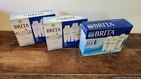 Photo of three unopened Brita water filter boxes placed on a wooden surface, showing branding and packaging intact.