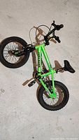 Full view of the green Tony Hawk Huckjam kids bicycle lying on the floor showing its size and condition including missing training wheels and black tires.