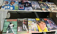 Photo showing a collection of assorted baseball books and magazines arranged on a shelf, featuring various baseball player images on the covers.