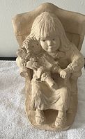 Photo showing a beige figurine sculpture of a seated girl holding a doll, made in 1987 from the Rock a Bye Baby collection by Dee Crowley