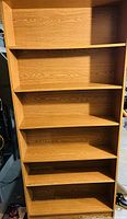 Front view of the wooden bookcase showing six empty shelves, light brown wood finish, rectangular shape.