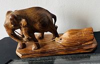 Side view of wooden elephant pulling a log sculpture on a wooden base showing details of elephant and log.