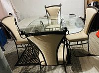Round glass top table with wrought iron base and four matching chairs with beige fabric seats.