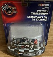Sealed package of NASCAR 1:43 scale Dale Earnhardt Victory Celebration diecast car showing front of packaging with checkered flag and racing figure.