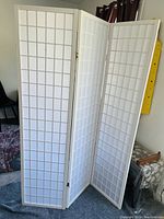 Front view of three-panel white folding room divider with grid pattern, standing upright indoors.