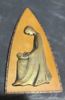 Wooden plaque with pewter figure of a seated person, full view against dark background.
