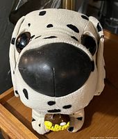 Close-up of the Dalmatian plush showing its head, black spots on white fabric, large black plastic nose and eyes, along with the brown collar with yellow text/design.