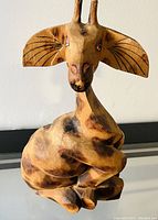 Front view of the whimsical wooden giraffe sculpture showing detailed face, painted eyes, ears with black lines, and body shape.