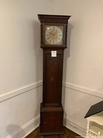 Full front view of oak longcase grandfather clock against white wall showing entire case and brass dial