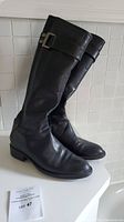 Side view of the black knee-high leather boots showing buckle strap detail and slight creases on leather.