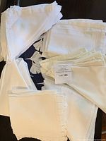 Photo showcasing assorted white cloth and linen napkins stacked together with navy blue round placemats partially visible underneath.