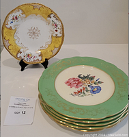 Yellow and white ornate Coalport dinner plate displayed on stand with stack of 5 green salad plates with floral center design