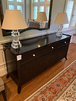 Front three-quarter view of dark brown wooden sideboard with fluted front panels and two lamps on top