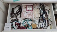 Wide view of multiple beaded and jeweled necklaces, assorted styles and colors in drawer