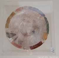 Front view of the round paper mache sculpture in an acrylic case showing the muted color blocks and textural surface.