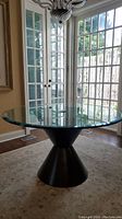 Full view of round glass kitchen table in room with windows and chandelier