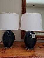 Pair of navy blue ceramic table lamps with white shades on wooden surface with mirror behind