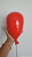 Hand holding front of glossy red ceramic balloon to show scale