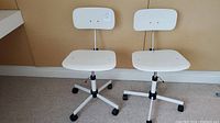 Front view of pair of white mid-century modern adjustable chairs against beige wall.