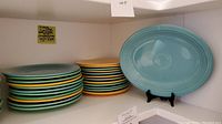 Stacks of round plates in green, yellow and turquoise with a turquoise oval platter on display stand