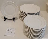 Two stacks of white porcelain plates: one stack of 13 larger plates, one stack of 14 smaller plates; single plate on stand and auction lot sign.