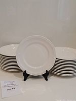 Front view of the stack of white porcelain plates with one plate displayed on a stand, elegant embossed edges visible.