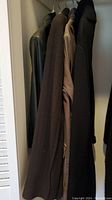 Photo showing four women's jackets hanging in a closet, colors brown, taupe, black, and dark material.