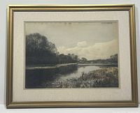 Framed watercolour landscape painting showing river, trees, and sky under glass with gold-toned frame.