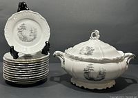 12 vintage bread and butter plates stacked with one displayed on stand, next to an ornate covered vegetable dish with lid.