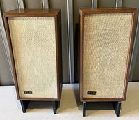 Front angle view of both vintage KLH Model Seventeen speakers on black stands, showing wood grain and beige fabric grills bearing KLH logos.
