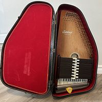 Autoharp seated in open black hard case with red velvet interior