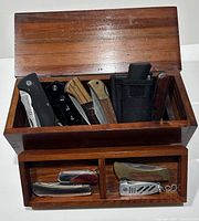 Top view showing wooden box open and filled with knives and box cutters inside and in drawer