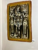 Full view of papyrus art showing three standing ancient Egyptian figures in metallic brown and gold tones on a textured papyrus sheet.