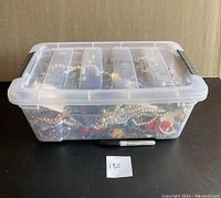 Plastic container full of costume jewelry with lid closed and sharpie pen for scale