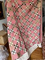 Handmade pink and brown patchwork quilt held up showing the front with various patterned squares
