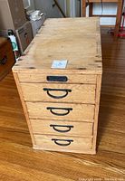 Front view of wooden 4 drawer cabinet showing four drawers with black metal handles and a side carrying handle.