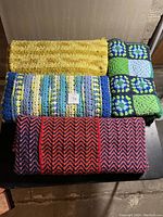 Four folded knitted afghans in yellow, red/pink/blue, blue/green, and blue/yellow colors.